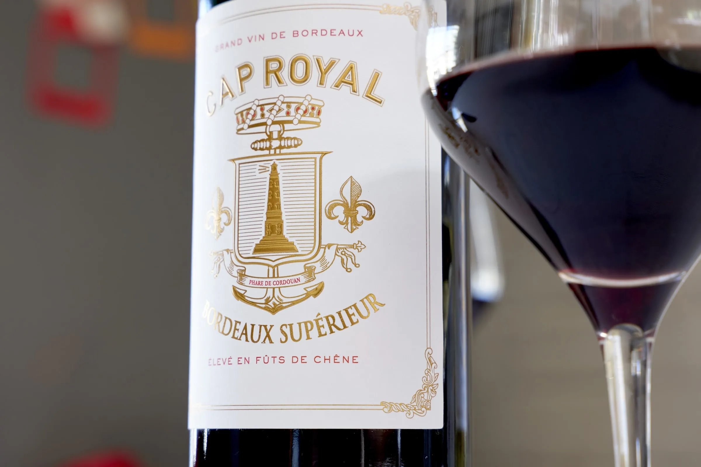 Détail de l'étiquette dorée de Cap Royal Bordeaux Supérieur, à côté d'un verre de vin rouge
