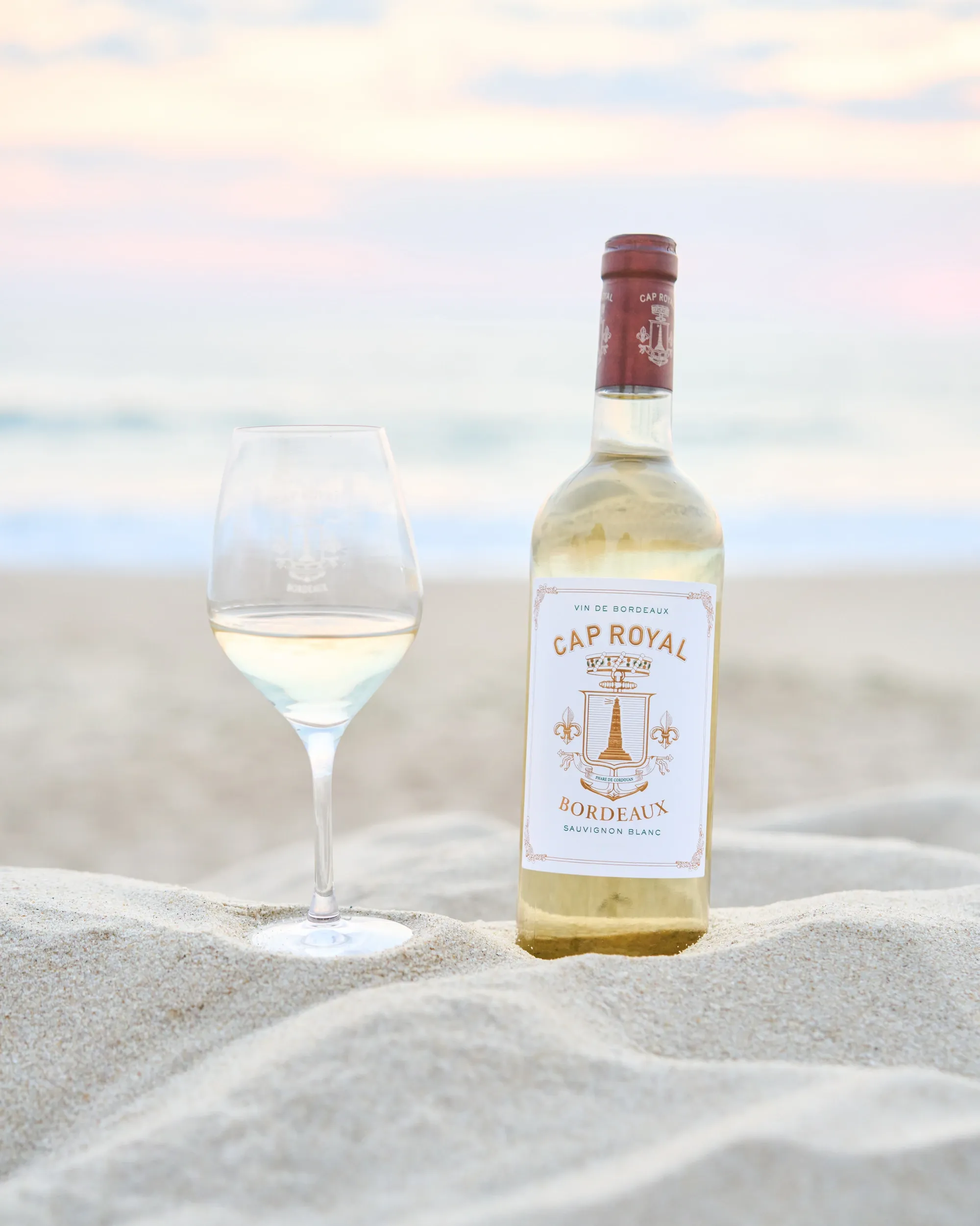 Bouteille et verre de Cap Royal Sauvignon Blanc sur le sable, au coucher du soleil